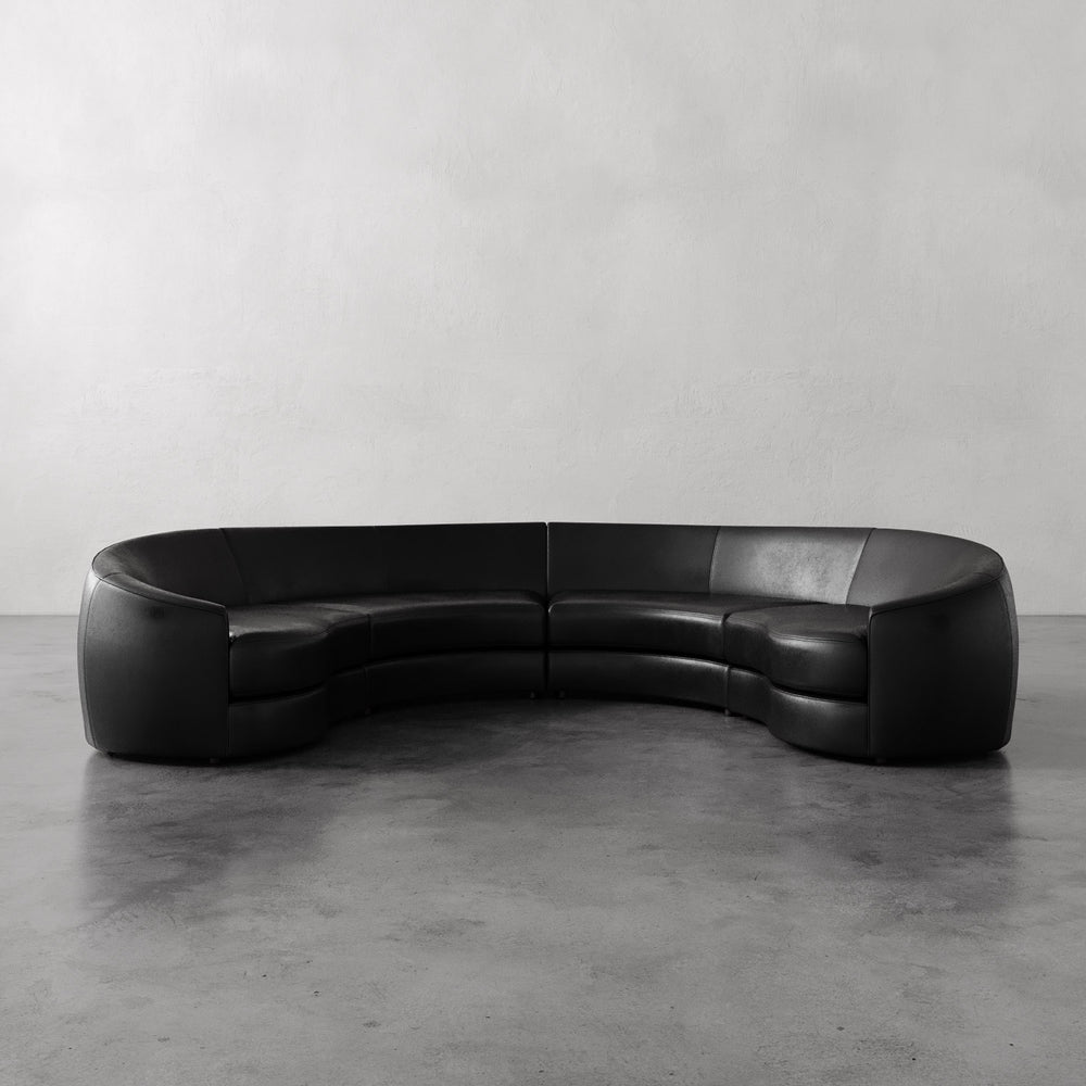 Lemieux et Cie Rulmann 4-Piece Sectional in black leather, curved modular sofa on polished concrete floor against white walls.