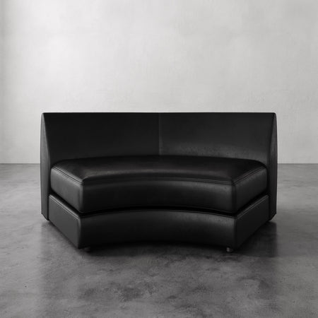 Lemieux et Cie Rulmann Wedge in black leather, curved sectional seating with geometric high back, shown on polished concrete floor against neutral walls.