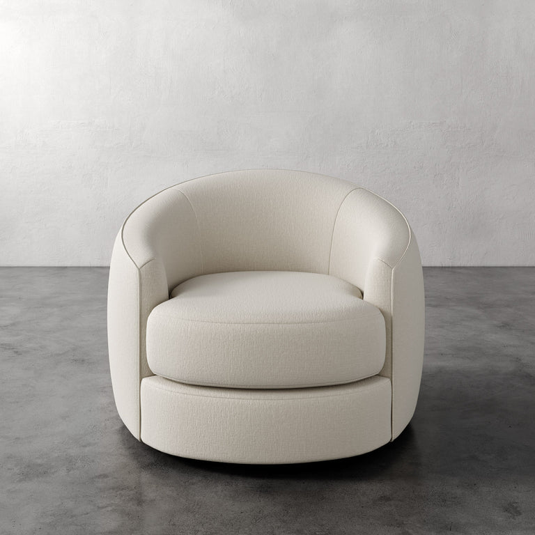 Lemieux et Cie Rulmann Swivel Chair in ivory, rounded barrel-back lounge chair on polished concrete floor with textured plaster walls.