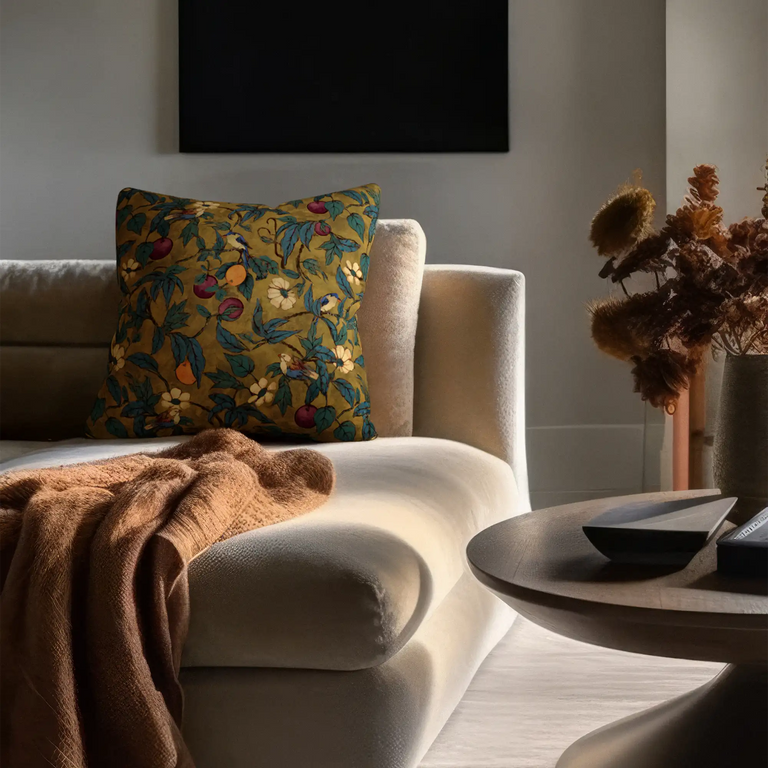Lemieux et Cie Plum Garden Velvet Pillow in ochre with fruit and floral motif, decorative pillow on ivory sofa in neutral-walled sitting room with warm daylight.