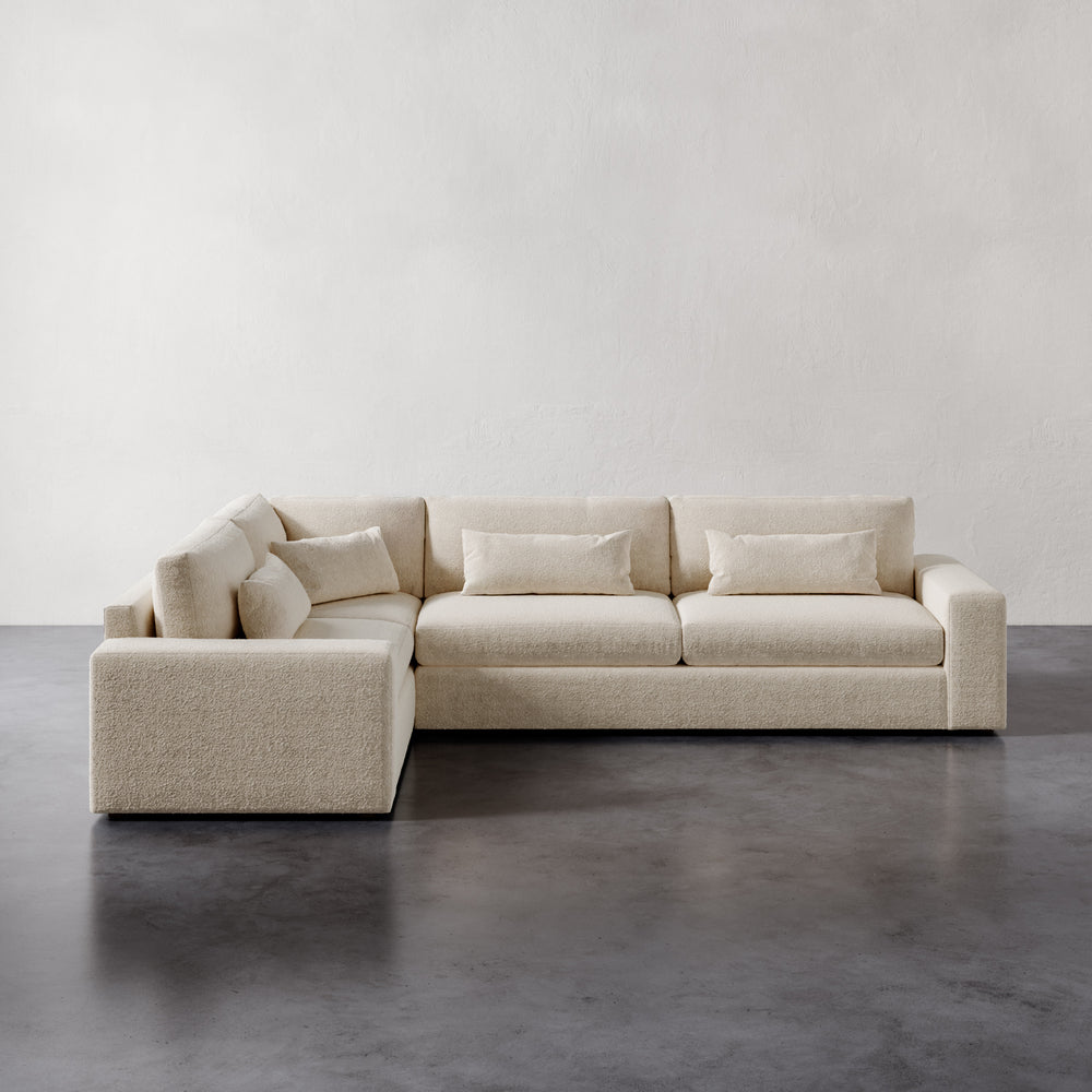 Lemieux et Cie Lacroix Right Arm Sectional in ivory bouclé, modular sofa with bolster pillows on charcoal concrete floors against neutral plaster walls.