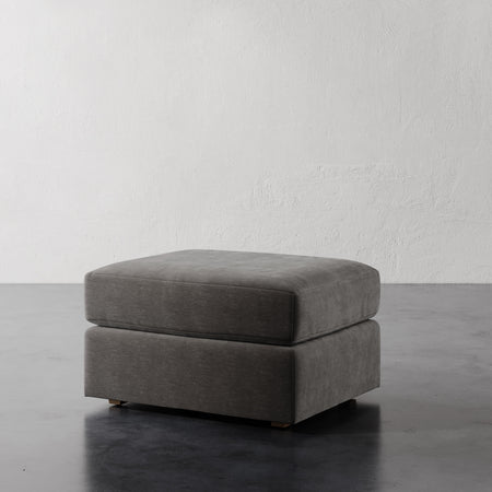 Lemieux et Cie Lacroix Ottoman, low-profile upholstered ottoman with clean rectilinear form, shown on concrete floor against textured white plaster wall.