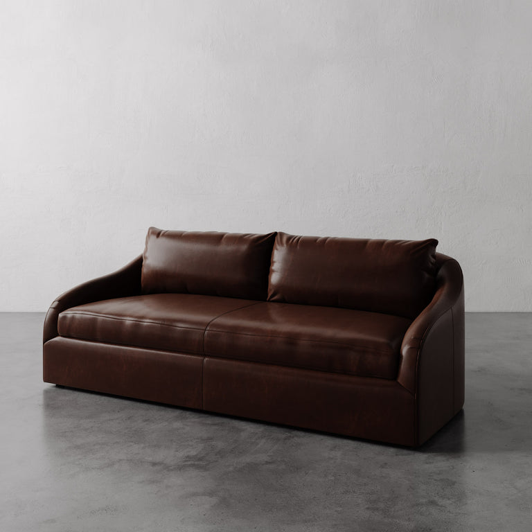 Lemieux Et Cie Dark Brown Rousseau Leather Sofa on a gray floor with a plain white wall background.