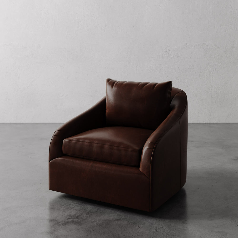 Lemieux et Cie Rousseau Swivel Chair in warm brown leather, low-profile lounge chair with rounded arms, shown on concrete floor against white plaster wall.