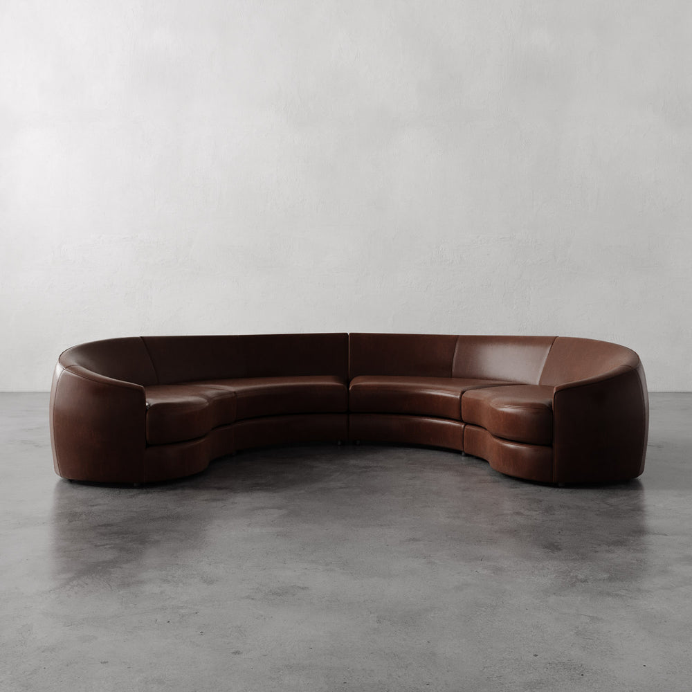Lemieux et Cie Rulmann 4-Piece Sectional in warm brown leather, curved modular sofa on polished concrete floor in neutral room.