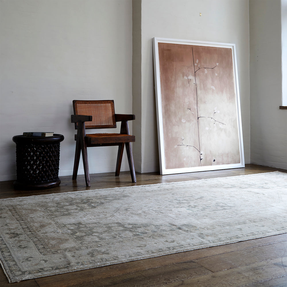 Lemieux et Cie Lemieux et Rie vintage Shiraz rug in soft gray and taupe with geometric tribal patterns, hand-knotted wool carpet shown on wood floors beside a caned chair in a neutral-walled room.