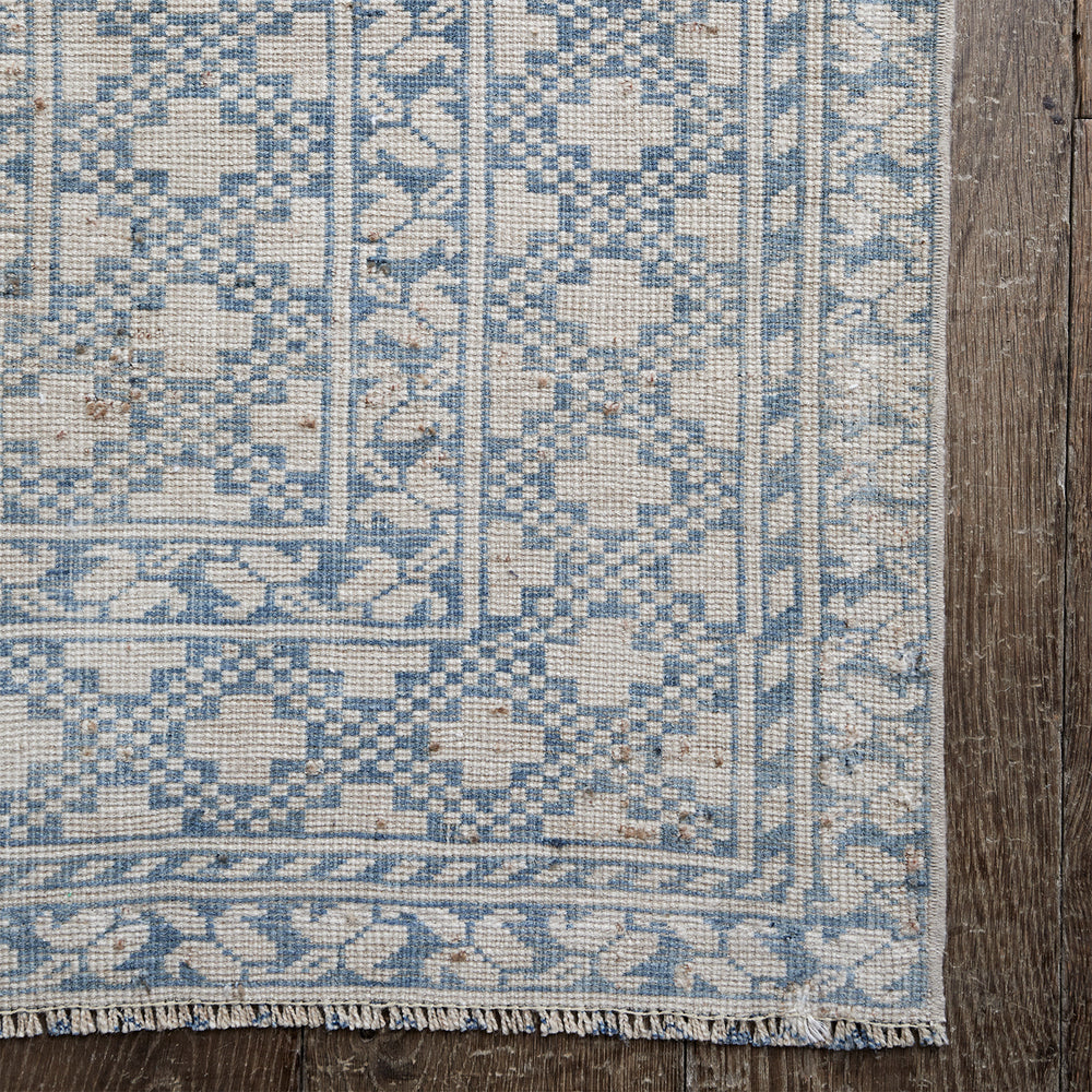 Lemieux et Cie vintage rug in blue and ivory geometric motifs, handwoven circa 1960, detail of corner showing fringe on aged wood floor.