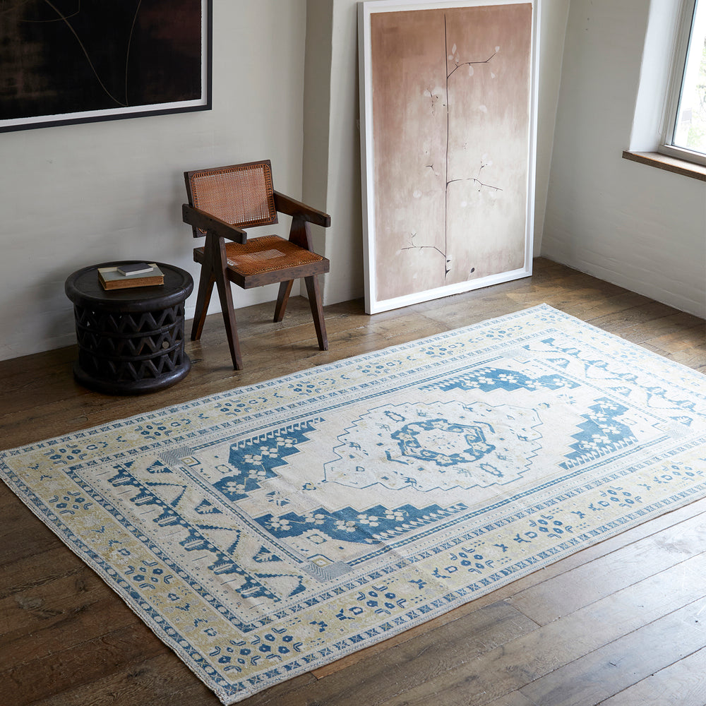Lemieux et Cie Anatolian village rug in blue and ivory geometric pattern, handwoven wool shown on light wood floors beside rattan chair and carved side table.