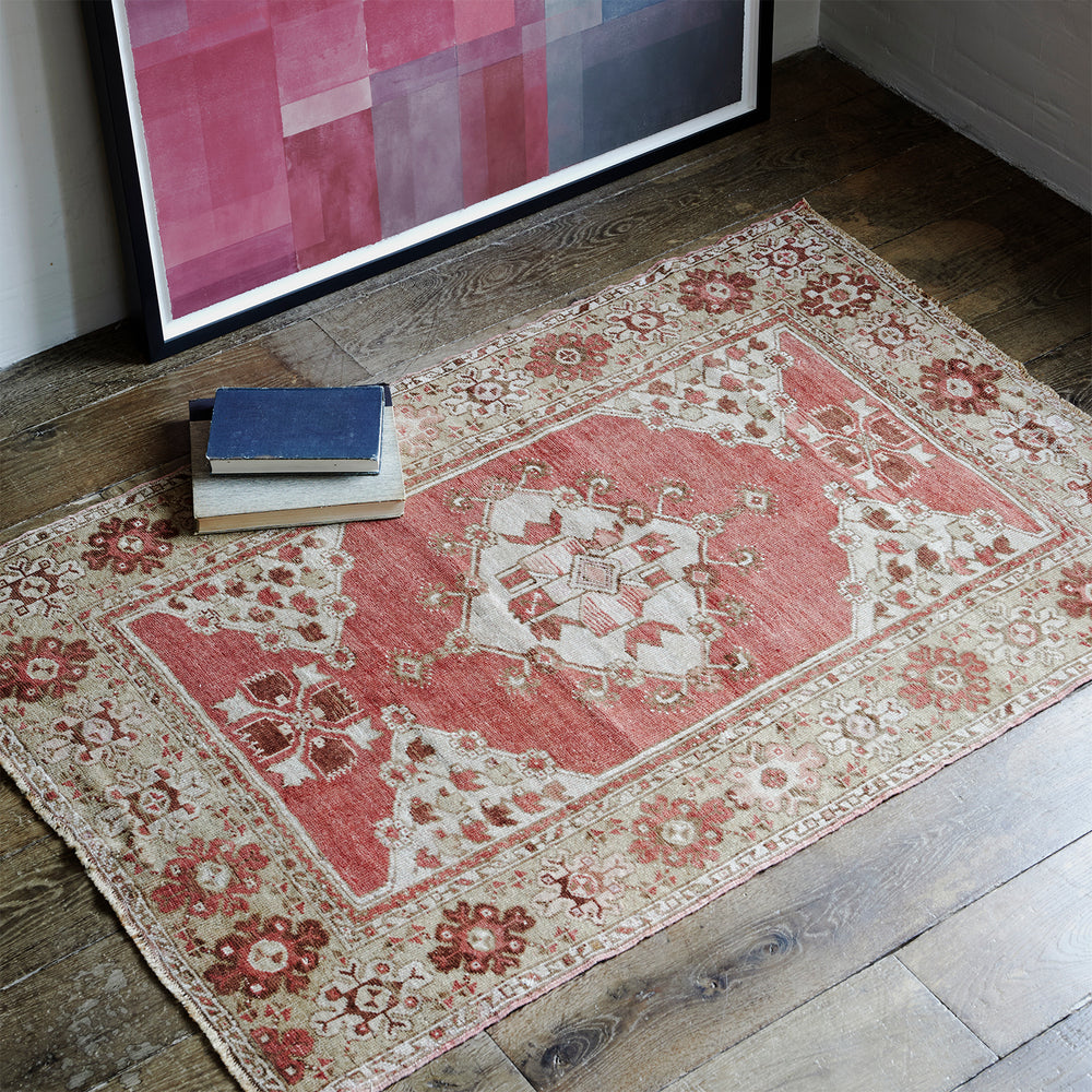 Lemieux et Cie Anatolian Village Rug in coral and neutral tones, vintage geometric medallion pattern on dark wood floors beneath framed abstract artwork.