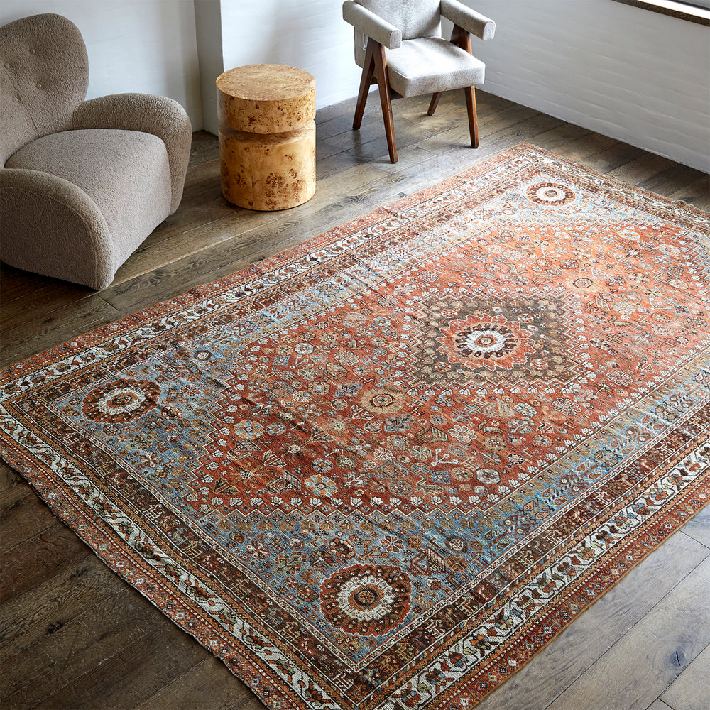 Lemieux et Cie Anatolian village rug in rust, blue and ivory with geometric medallion pattern, vintage hand-knotted wool shown on wide-plank wood floors in a sitting room.