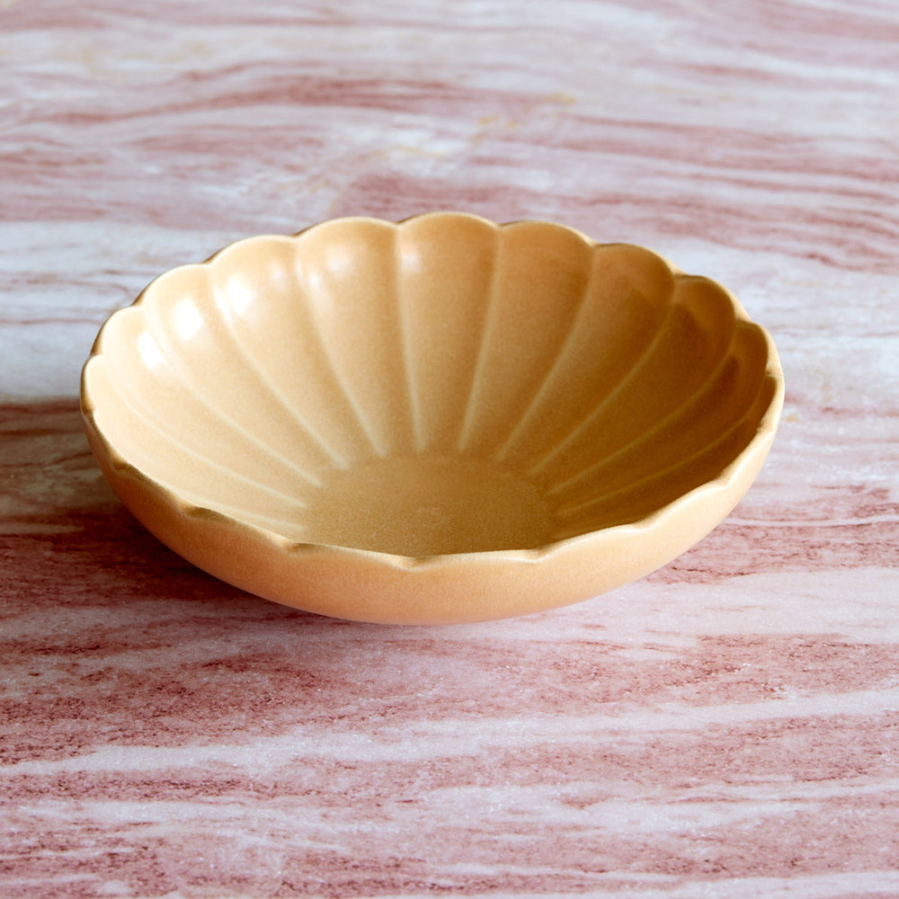 Lemieux et Cie Dhalia Stoneware Pasta Bowl in camel, scalloped ceramic bowl shown on pink-veined marble surface in soft natural light.