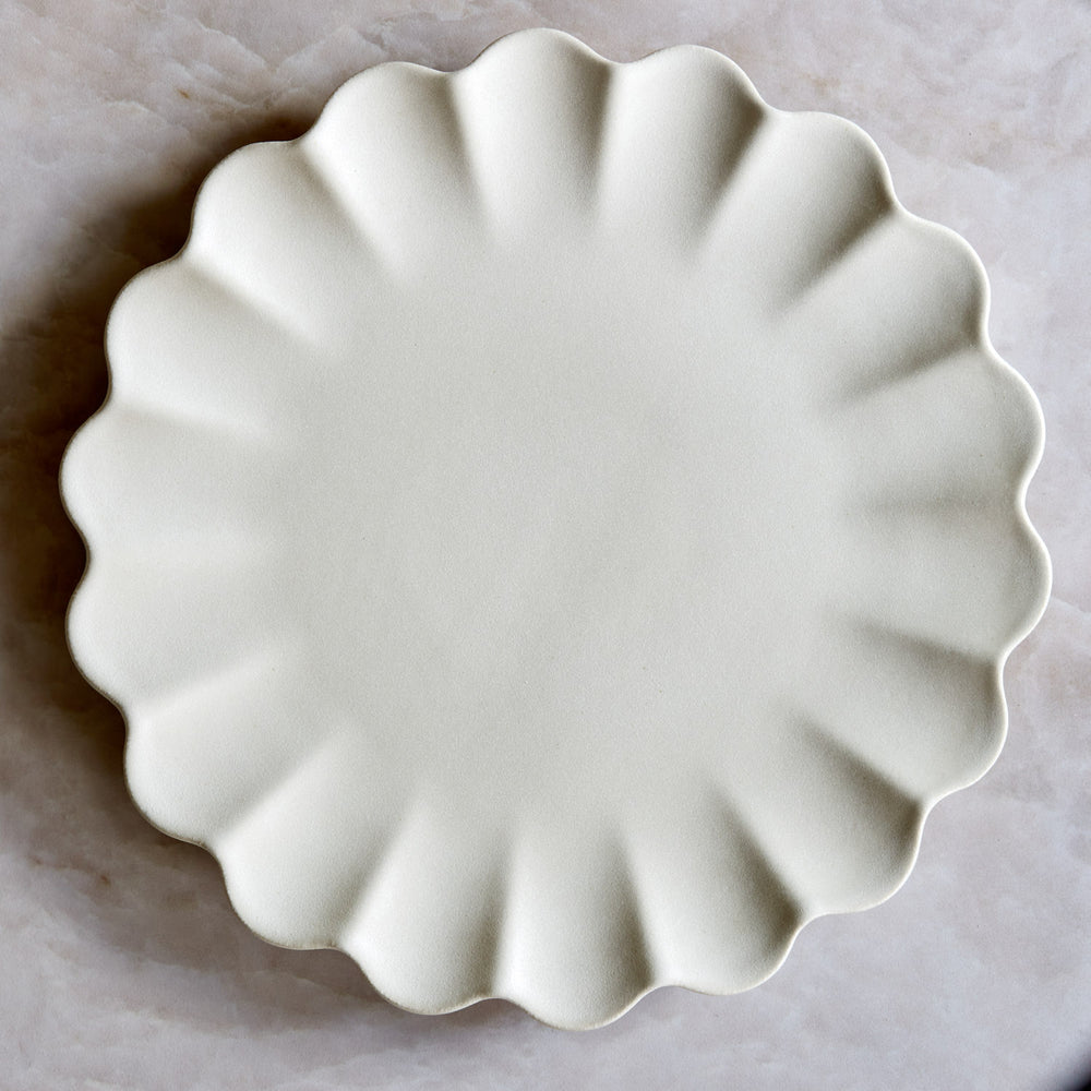 Lemieux et Cie Dhalia Stoneware Dinner Plate in white, scalloped ceramic plate with fluted edges, shown on pale marble surface.