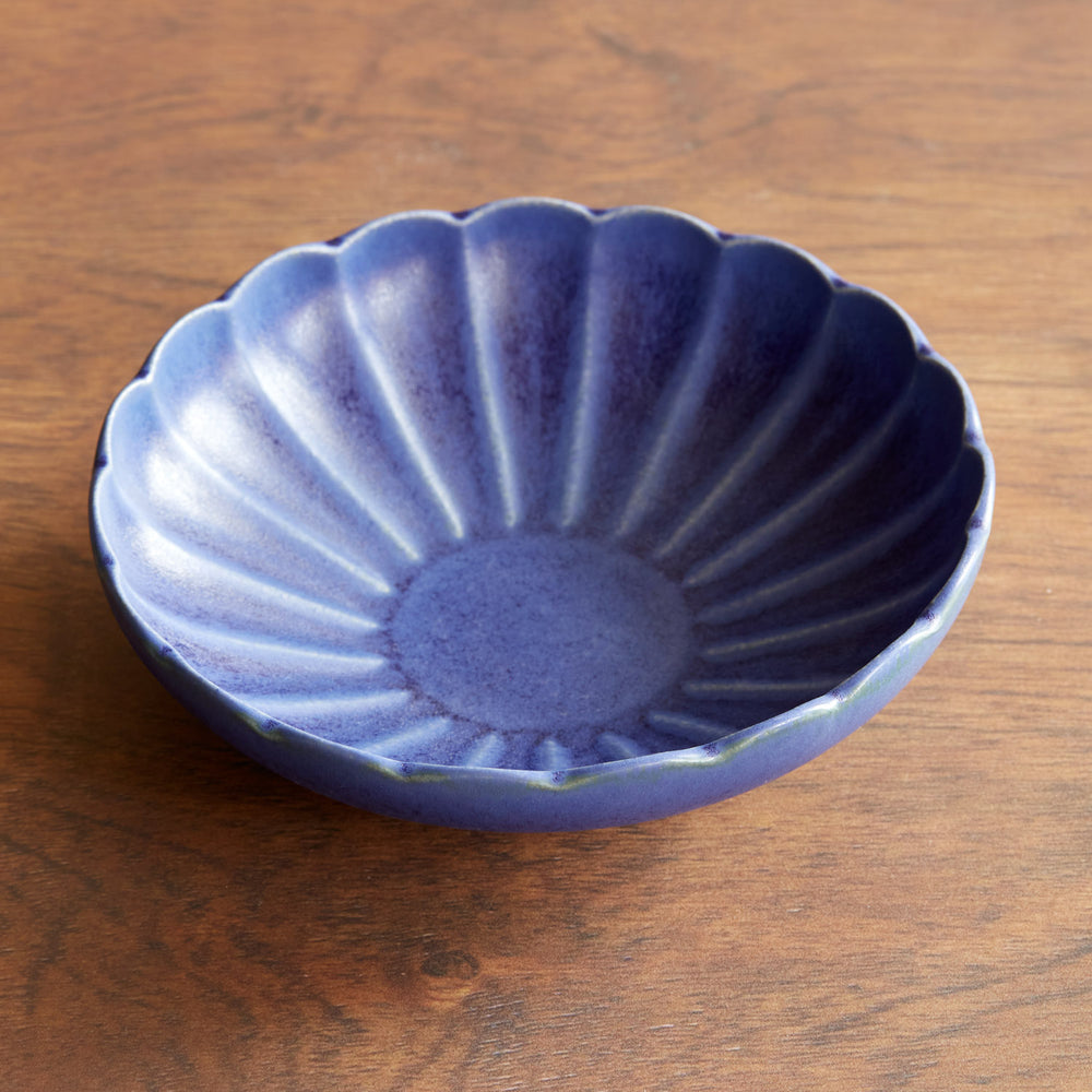 Lemieux et Cie Dhalia Stoneware Pasta Bowl in blue ceramic with scalloped edges, shown on warm wood table surface.