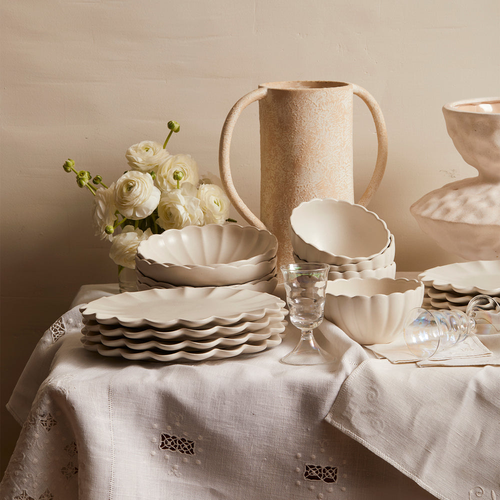 Lemieux et Cie Dhalia Stoneware 16-Piece Dinnerware Set in white, scalloped plates and bowls with ceramic vase, arranged on linen tablecloth