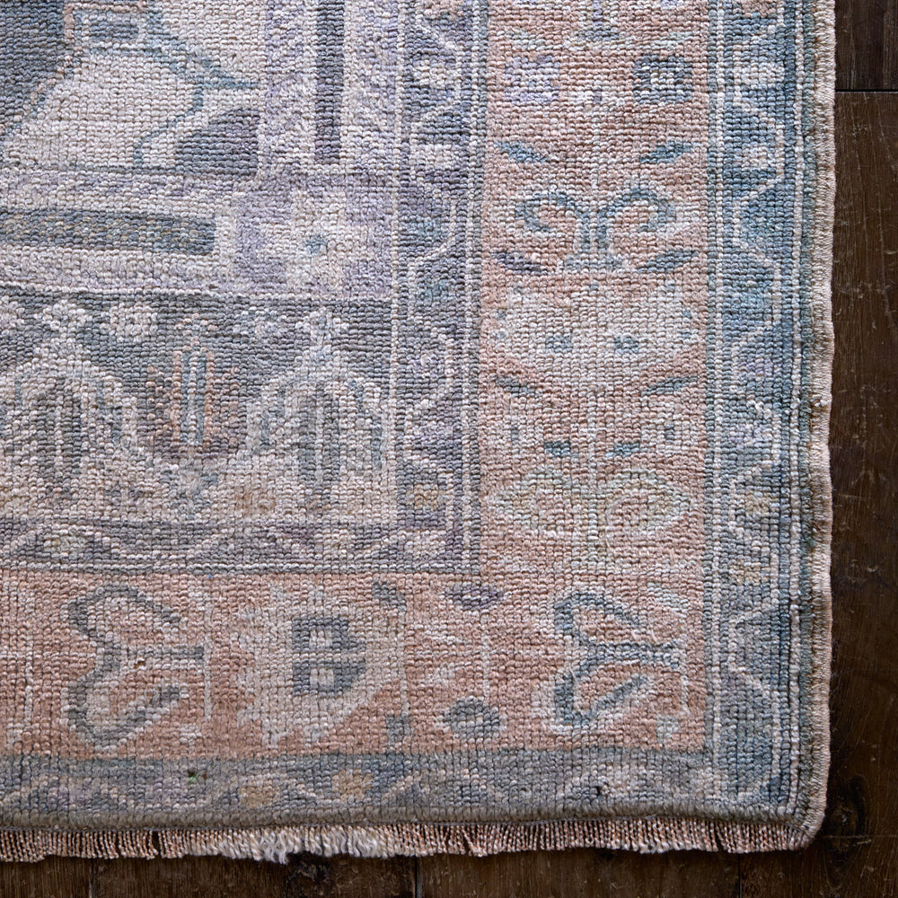 Lemieux et Cie Vintage 1960's Anatolian rug in blush, blue and grey tones, woven corner detail shown on dark wood flooring.