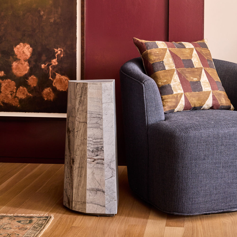Lemieux et Cie Mille Pillar Side Table in blue forest marble, geometric side table styled beside a charcoal sofa with warm wood floors and red walls.
