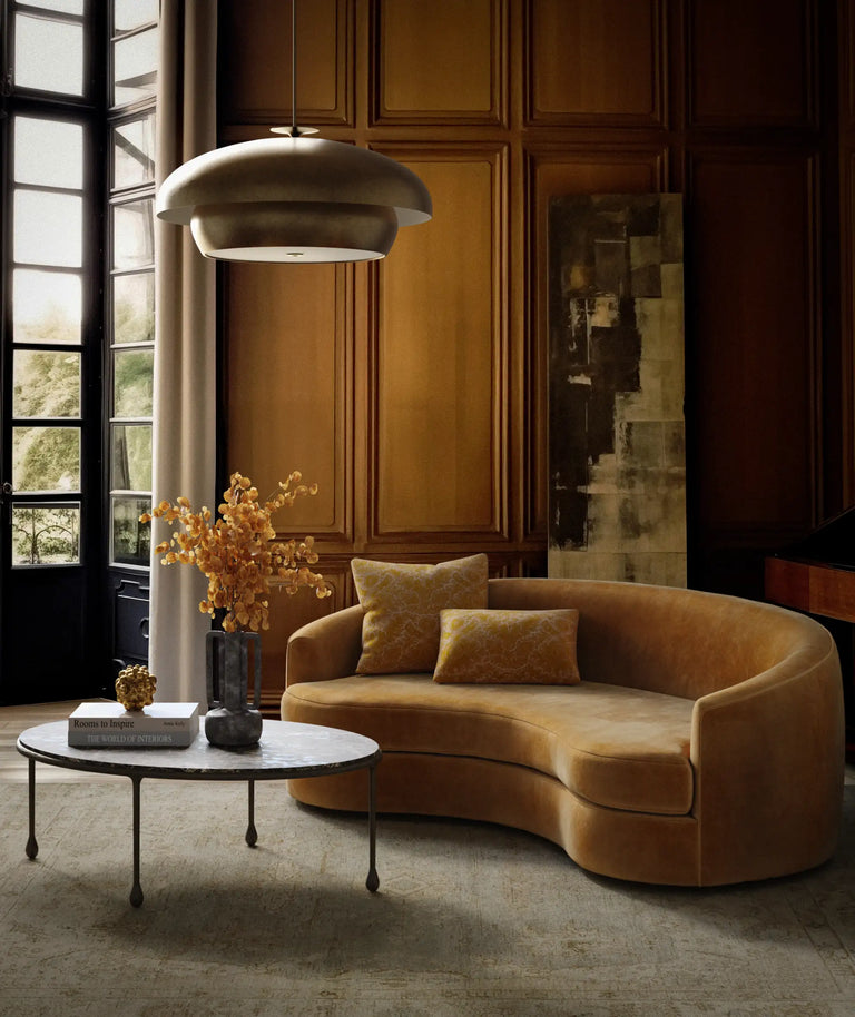 Lemieux et Cie Solene Chandelier, sculptural rounded pendant in warm tones, hung above curved sofa in wood-paneled sitting room with stone floor.