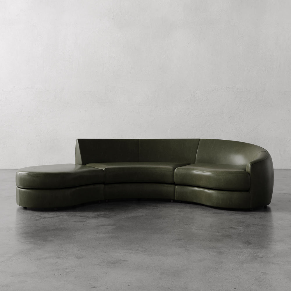 Lemieux et Cie Rulmann Right Sectional in deep olive green leather, curved modular sofa on polished concrete floor against neutral plaster walls.