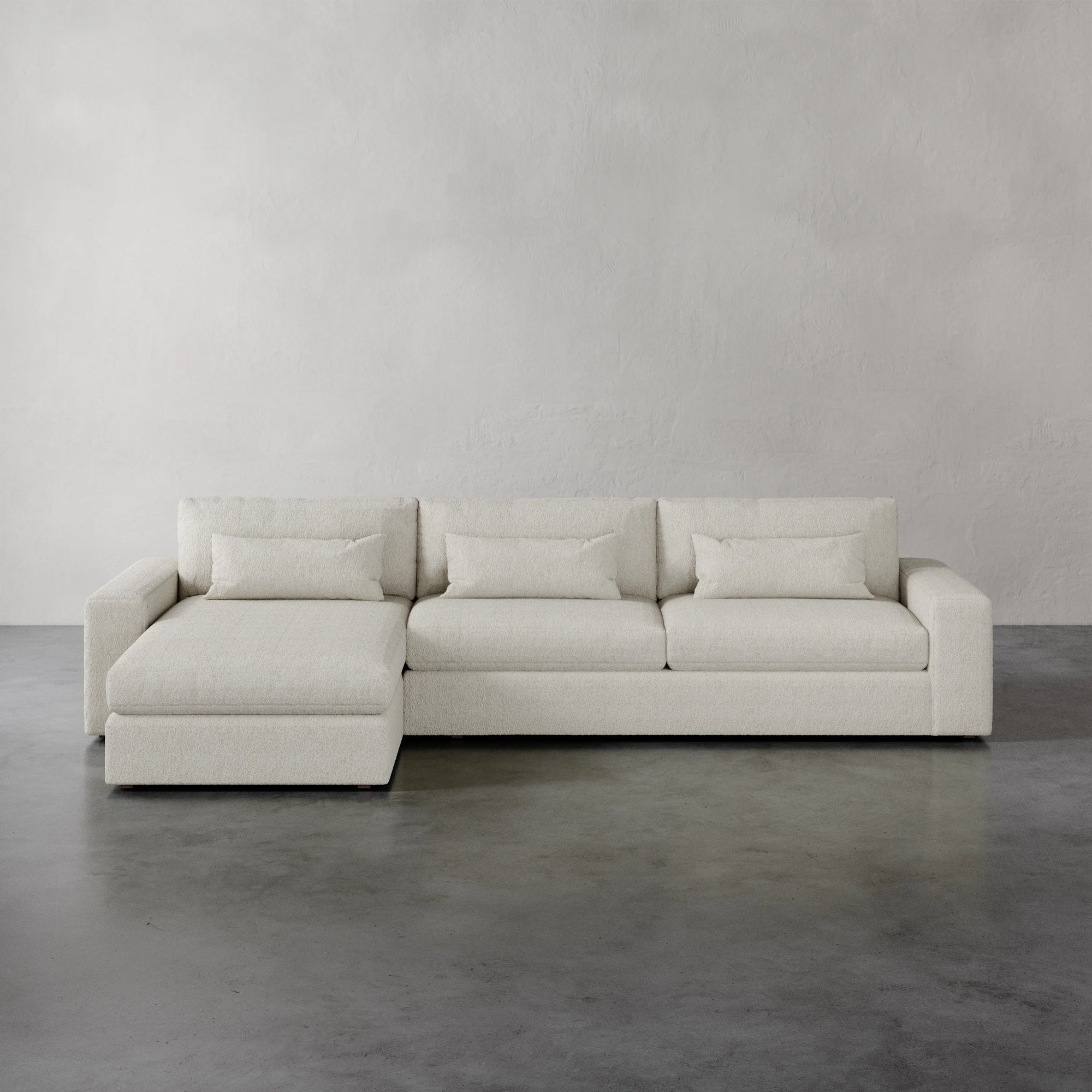 Lemieux et Cie Lacroix Left Chaise Sectional in ivory, low-profile modular sofa with chaise extension, shown on polished concrete floor against neutral plaster walls.