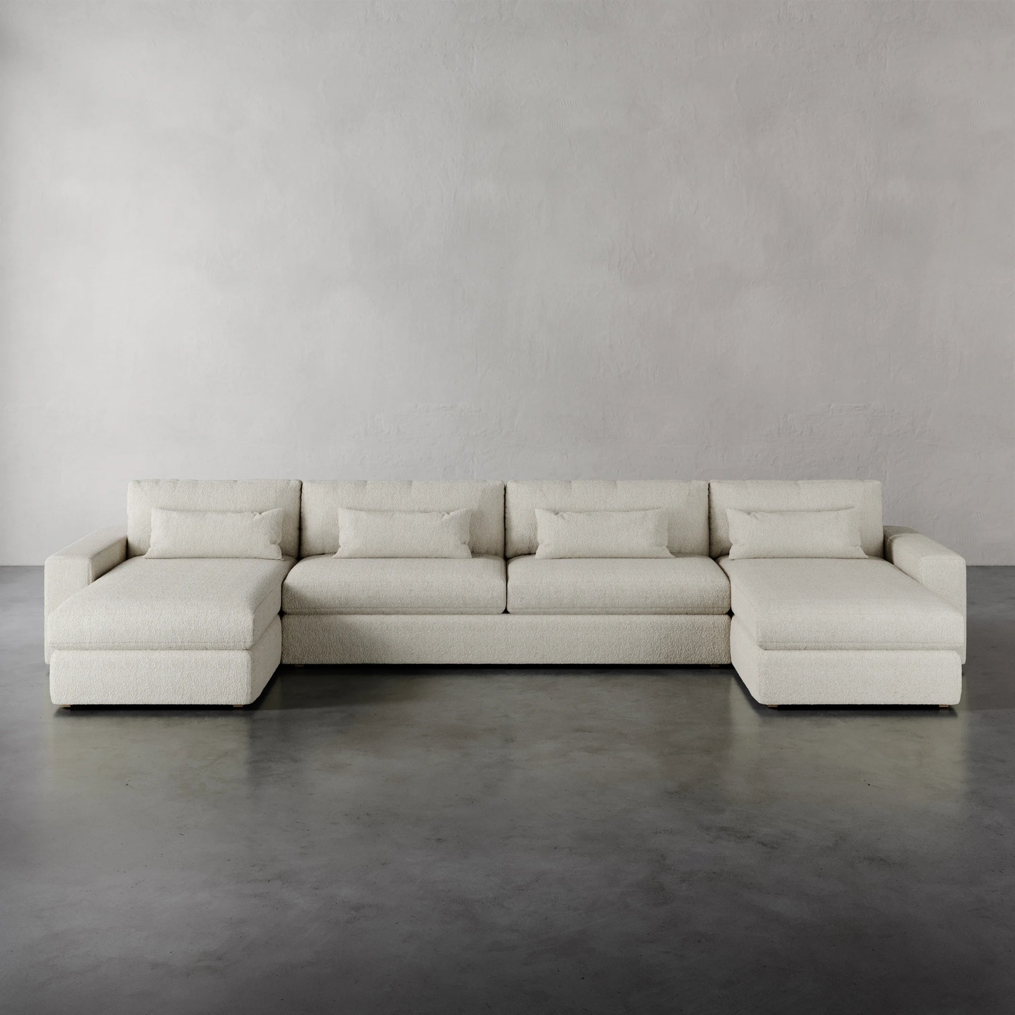 Lemieux et Cie Lacroix Sofa Chaise & A Half U-Sectional in ivory, low-profile modular seating with deep cushions, shown on polished concrete floor against textured plaster walls.