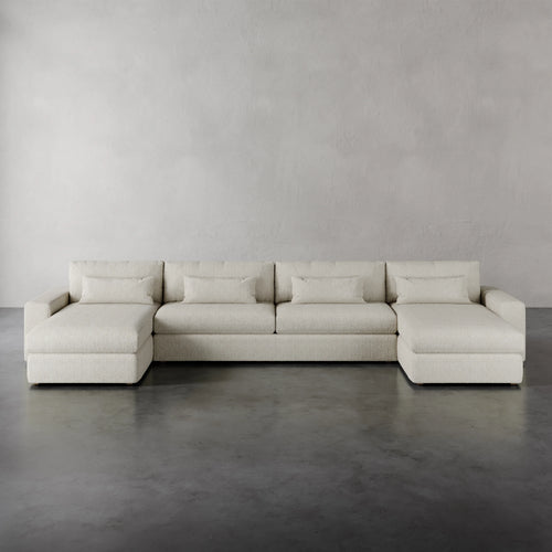 Lemieux et Cie Lacroix Sofa Chaise & A Half U-Sectional in ivory, low-profile modular seating with deep cushions, shown on polished concrete floor against textured plaster walls.
