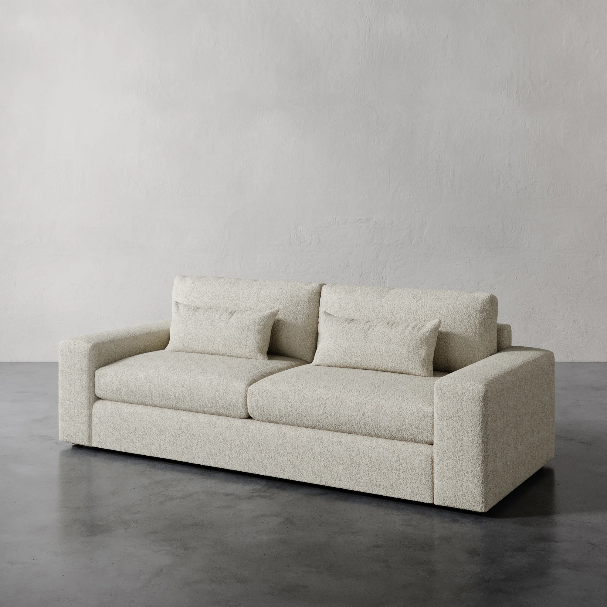 Lemieux et Cie Lacroix Sofa in cream bouclé, low-profile sofa with geometric form, set on concrete floor against textured plaster walls.