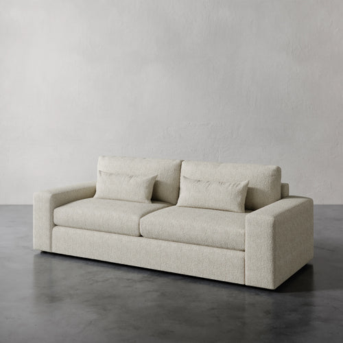 Lemieux et Cie Lacroix Sofa in cream bouclé, low-profile sofa with geometric form, set on concrete floor against textured plaster walls.