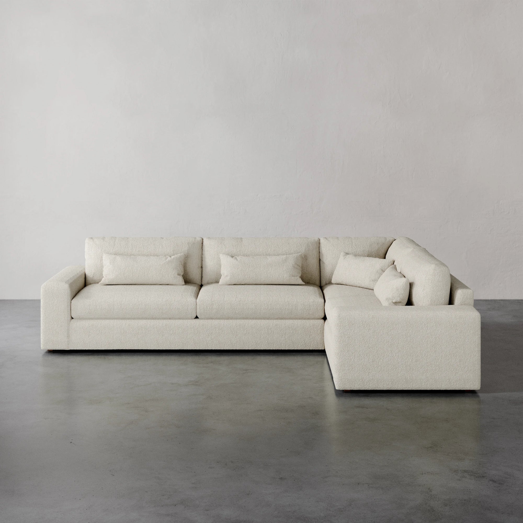 Lemieux et Cie Lacroix Left Arm Sectional in ivory, modular sofa with deep cushions and bolster pillows, shown on concrete floor against neutral walls.