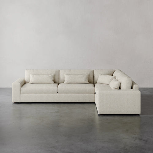 Lemieux et Cie Lacroix Left Arm Sectional in ivory, modular sofa with deep cushions and bolster pillows, shown on concrete floor against neutral walls.