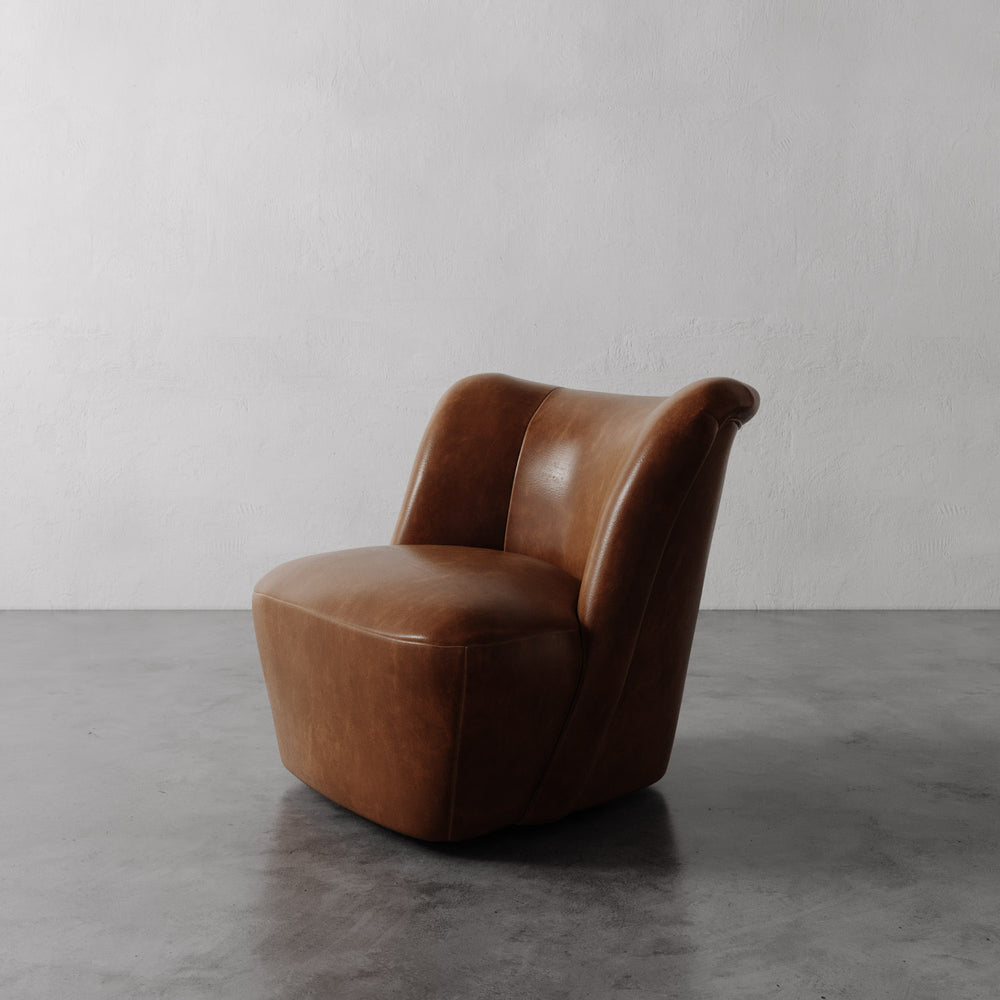 Lemieux et Cie Aurélie Leather Swivel Chair in warm tobacco leather, sculptural accent chair with rounded form on polished concrete floor against white plaster wall.
