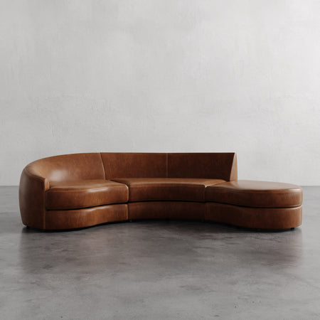 Lemieux et Cie Rulmann 3-Piece Left Sectional in warm cognac leather, curved low-profile sofa with chaise on polished concrete floor, neutral plaster walls.