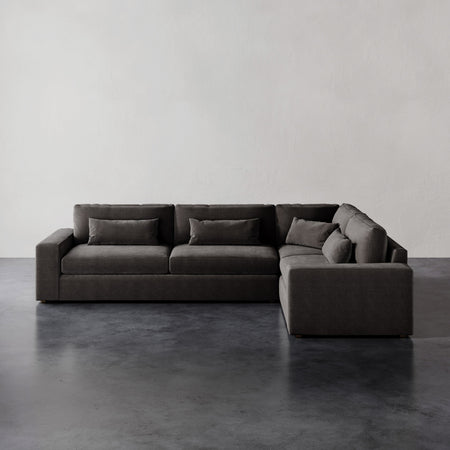 Lemieux et Cie Lacroix Left Arm Sectional in charcoal, modular sofa with deep proportions and bolster pillows, on dark concrete floor against white walls.