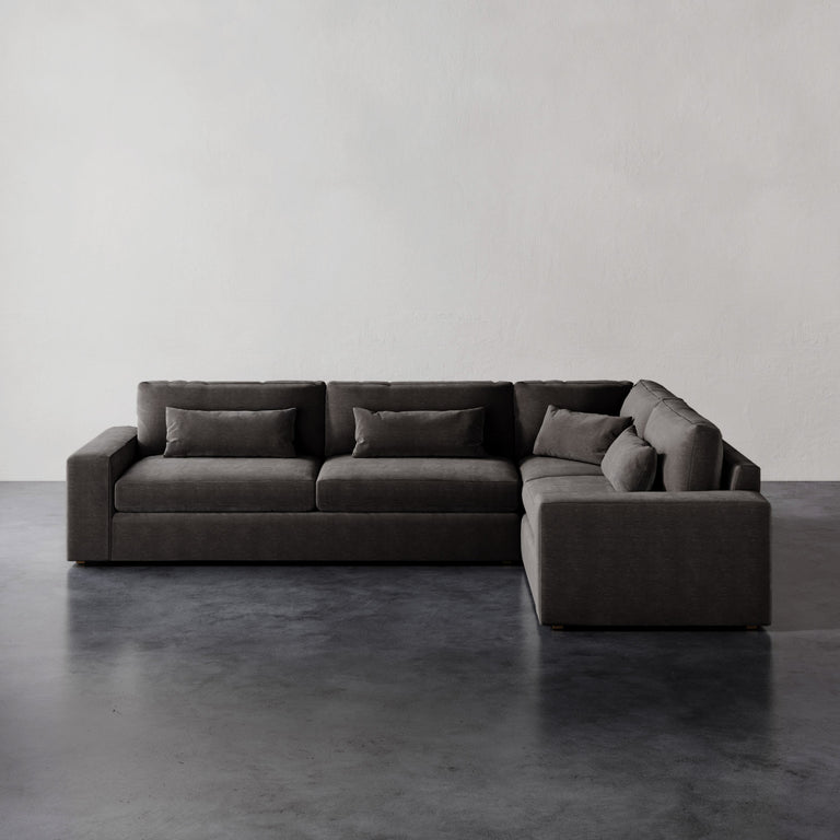 Lemieux et Cie Lacroix Left Arm Sectional in charcoal, modular sofa with deep proportions and bolster pillows, on dark concrete floor against white walls.