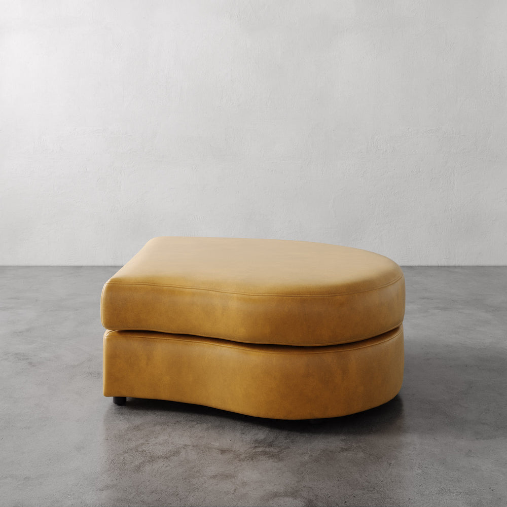 Lemieux et Cie Rulmann Right Ottoman in warm tobacco, low-profile curved ottoman on concrete floor against neutral plaster walls.