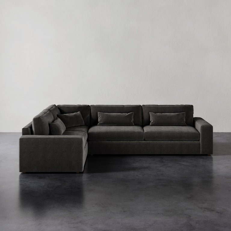 Lemieux et Cie Lacroix Right Arm Sectional in charcoal, modular L-shaped sofa with bolster pillows, on dark concrete floor against white walls.