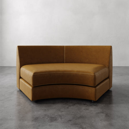 Lemieux et Cie Rulmann Leather Wedge in warm cognac, curved banquette seating with high back, shown on polished concrete floor against white walls.