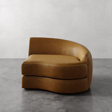 Lemieux et Cie Rulmann Right Arm Chair in warm caramel leather, sculptural curved form on polished concrete floor against white plaster wall.