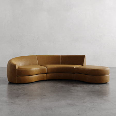 Lemieux et Cie Rulmann 3-Piece Left Sectional in warm tan leather, curved sofa with rounded cushions on polished concrete floor against white walls.