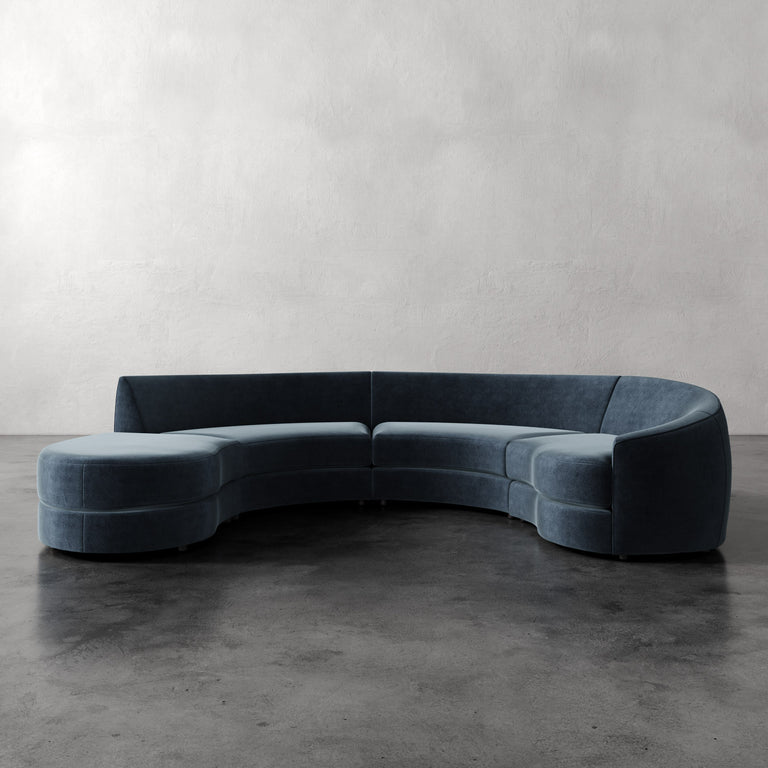 Lemieux et Cie Rulmann 4-Piece Right Sectional in slate blue, curved modular sofa on polished concrete floor against neutral plaster walls.