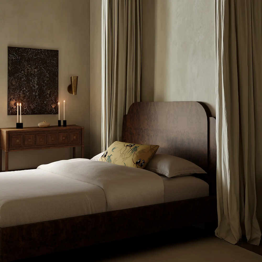 Lemieux et Cie Les Singes Velvet Pillow in warm gold with botanical and monkey motif, decorative pillow on upholstered bed in neutral bedroom with draped curtains.