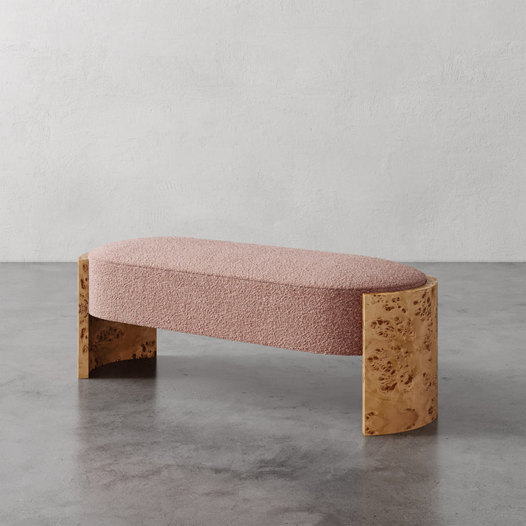Lemieux et Cie Benoit Custom Upholstered Bench in blush bouclé with curved Maple burl legs, shown on polished concrete floor against textured plaster wall.