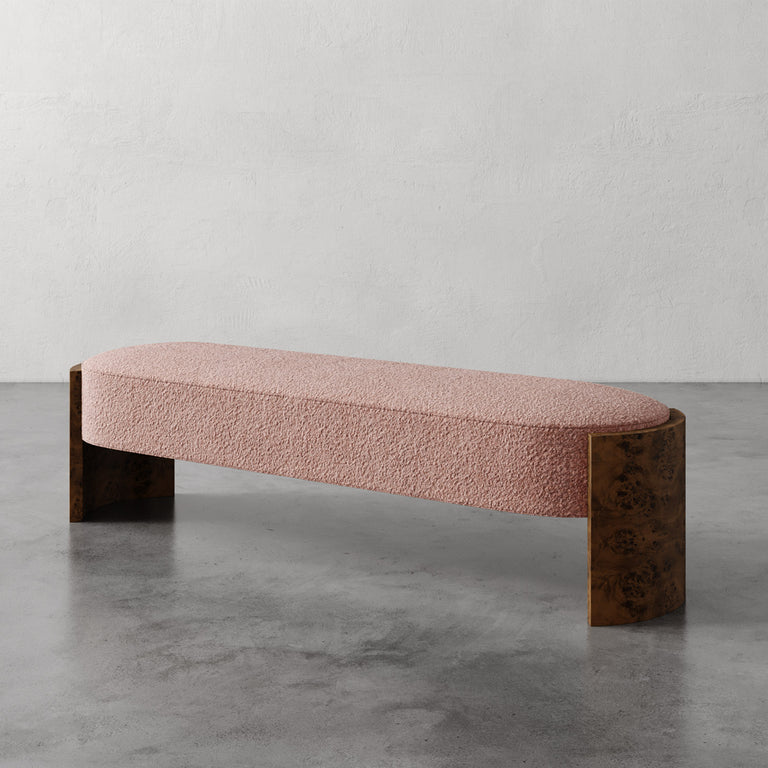 Lemieux et Cie Benoit Custom Upholstered Bench in blush bouclé with curved Maple burl legs, on polished concrete floor against textured plaster wall.