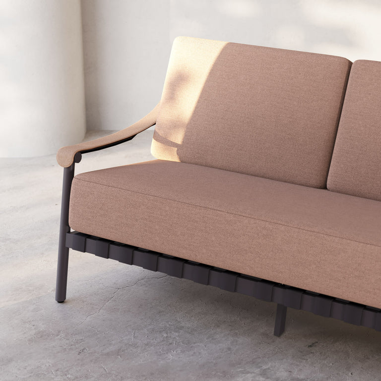 Lemieux Et Cie Hudson 3-Seat Sofa An outdoor sofa with gray fabric cushions, faux all-weather leather arms, and a powder coated aluminum frame, set in a contemporary indoor-outdoor setting with a tree in the background.