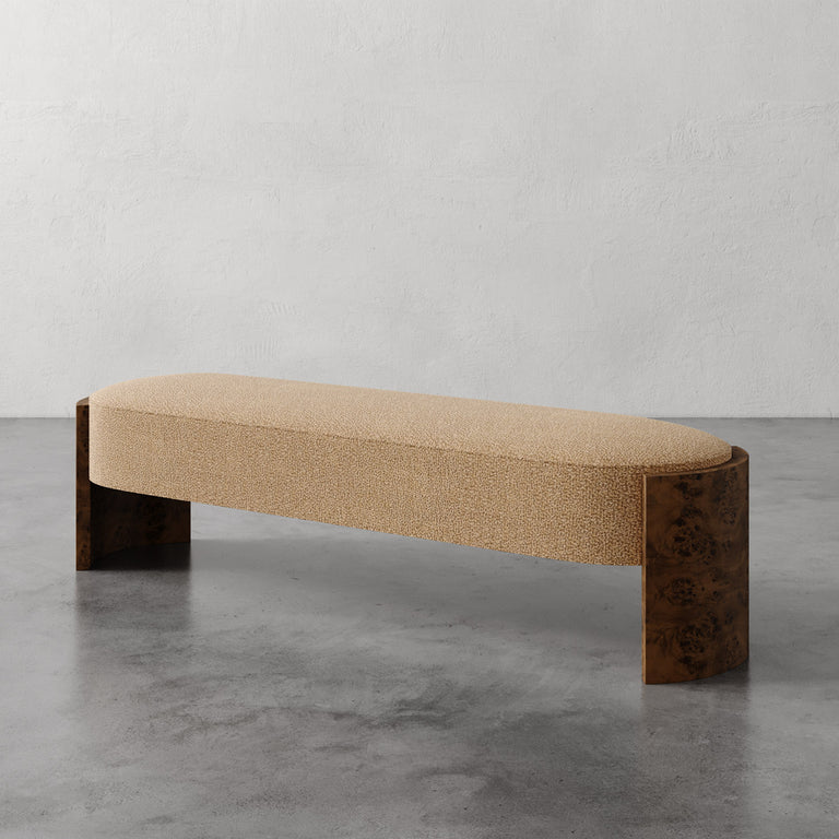 Lemieux et Cie Benoit Custom Upholstered Bench in textured neutral upholstery with curved Maple burl legs, shown on polished concrete floor against white plaster wall.