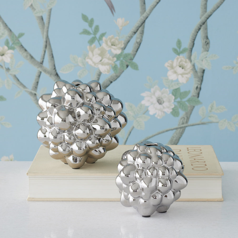 Lemieux et Cie Bubble Vase in polished silver electroplated finish, sculptural sphere form displayed on stacked books against blue chinoiserie wallpaper.