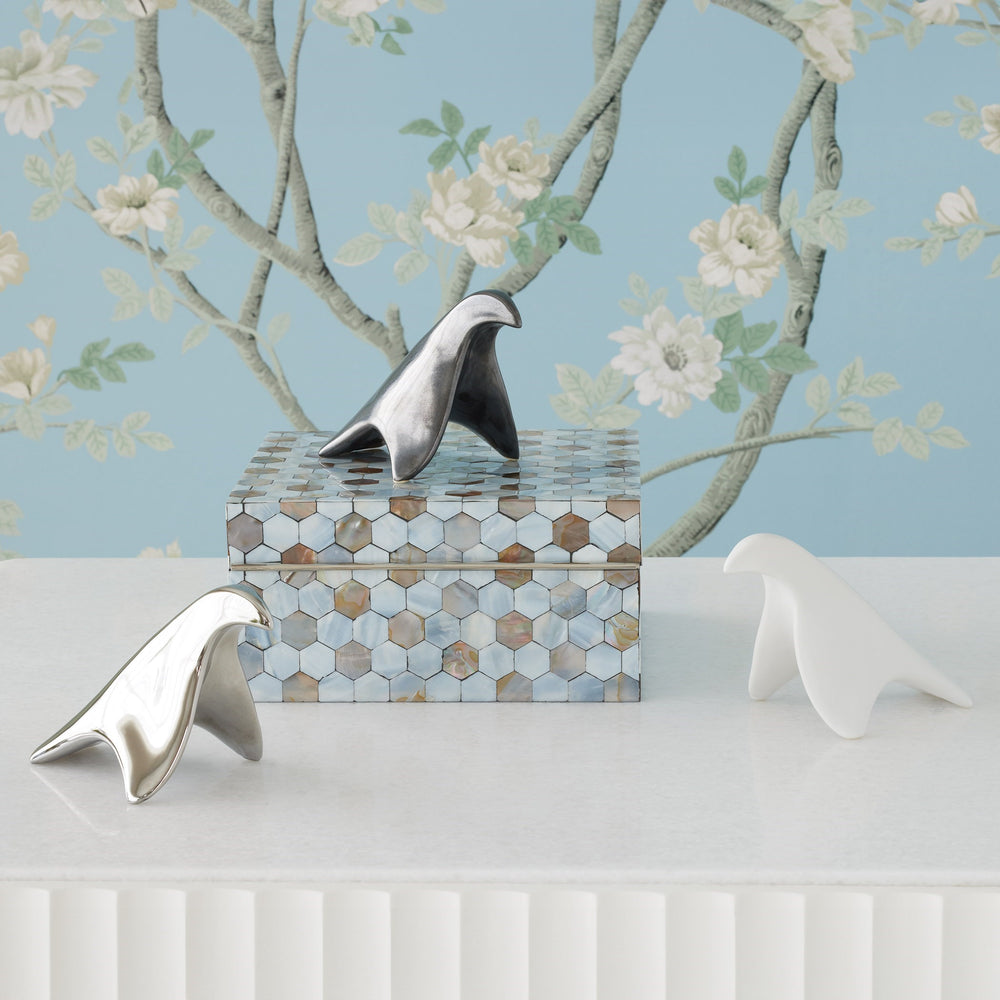 Lemieux et Cie bird sculptural objects arranged on mother-of-pearl hexagonal box against pale blue floral wallpaper with white branch motif in styled setting.