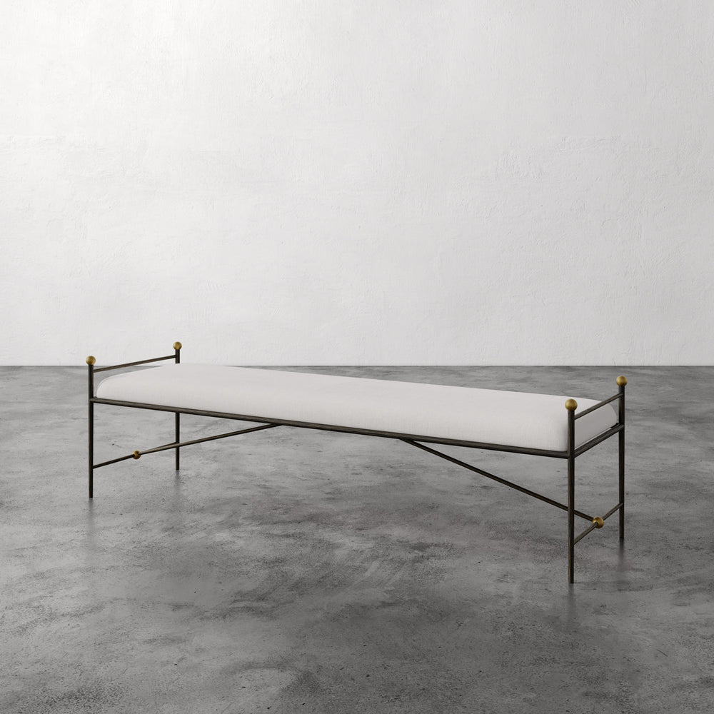 Lemieux et Cie Cambert Bench in white with bronze iron frame and aged brass accents, upholstered bench on polished concrete floor in neutral room.