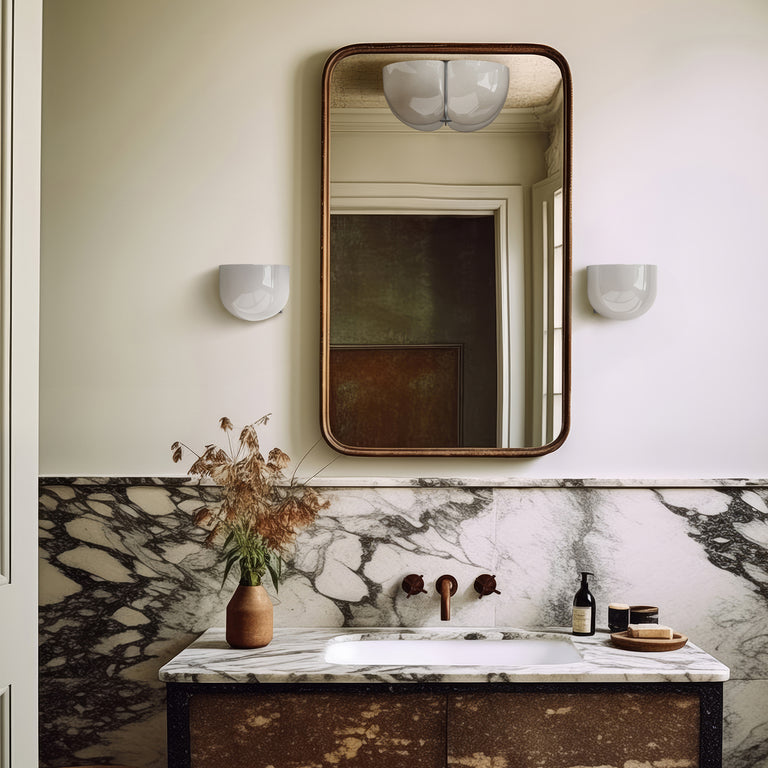 Lemieux et Cie Cheverny wall sconces in white, flanking a rounded mirror above marble vanity in a soft neutral bathroom with warm light.