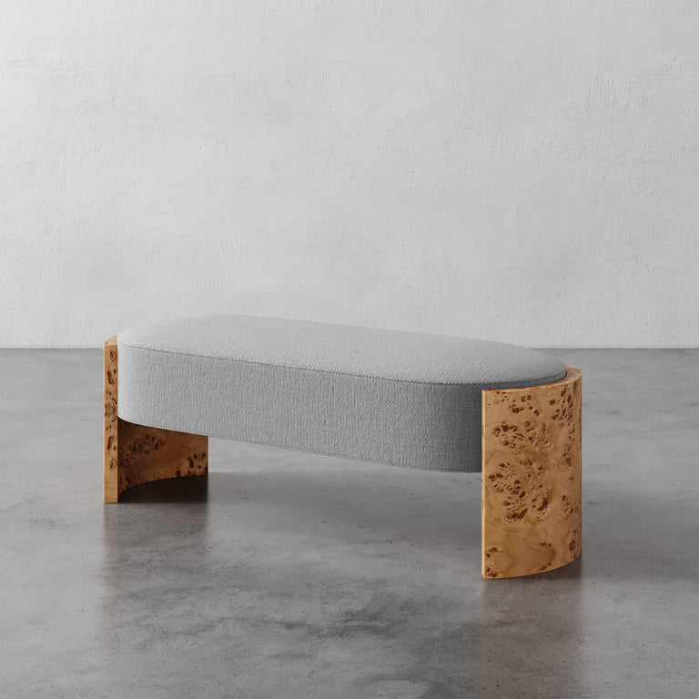 Lemieux et Cie Benoit Custom Upholstered Bench with curved maple burl legs and gray upholstered seat, shown on polished concrete floor against textured plaster walls.