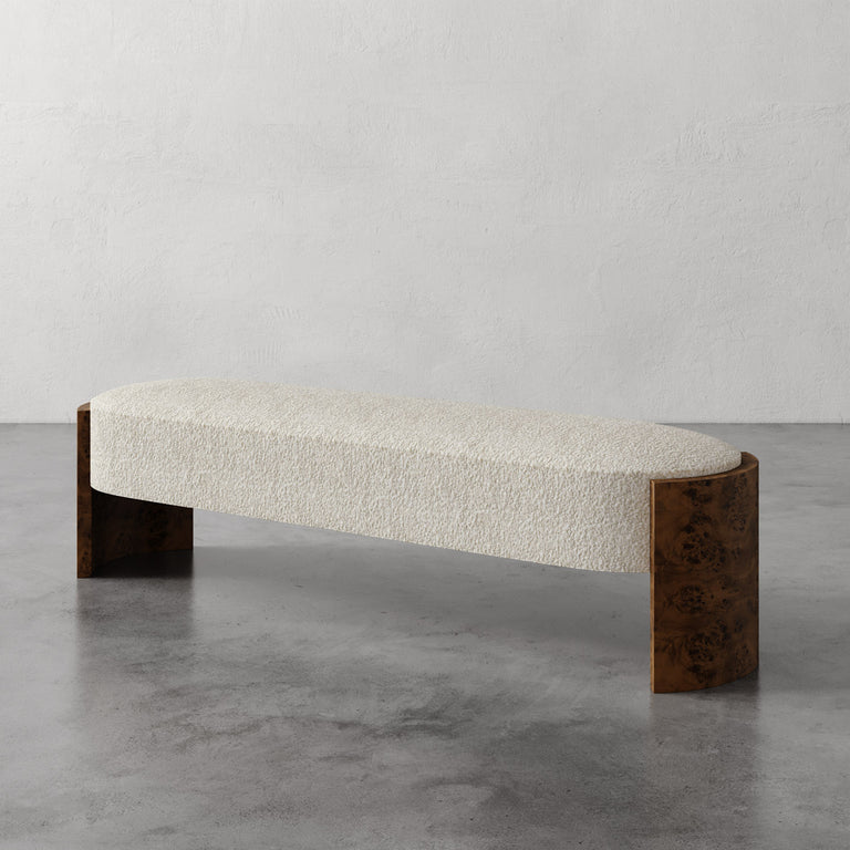 Lemieux et Cie Benoit upholstered bench in ivory bouclé with curved Maple burl legs, shown on polished concrete floor against neutral plaster walls.